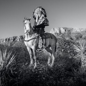 Apache by David Yarrow, a native american in feather headdress on a horse in the north american nature