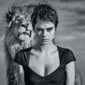 Cara Cigar by David Yarrow, Cara Delevingne in short hair and a bondage dress, standing in front of a lion