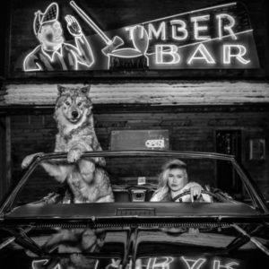 Coyote Ugly by David Yarrow, model and wolf sitting in a cabrio in front of a neon sign
