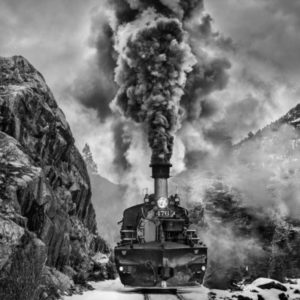 Vantage Point by David Yarrow, steam locomotive with heavy smoke between rocks, a native american with a gun standing on top of a hill looking down
