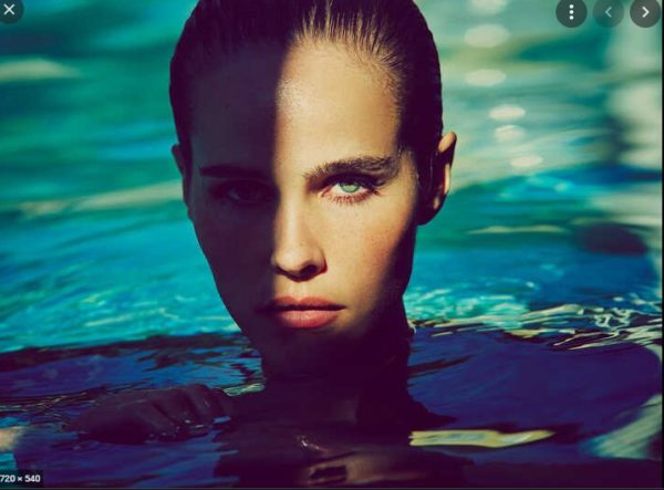 Deep End by Guy Aroch, Model with green eyes sticking her head out of blue and green water, partially covered in shadow