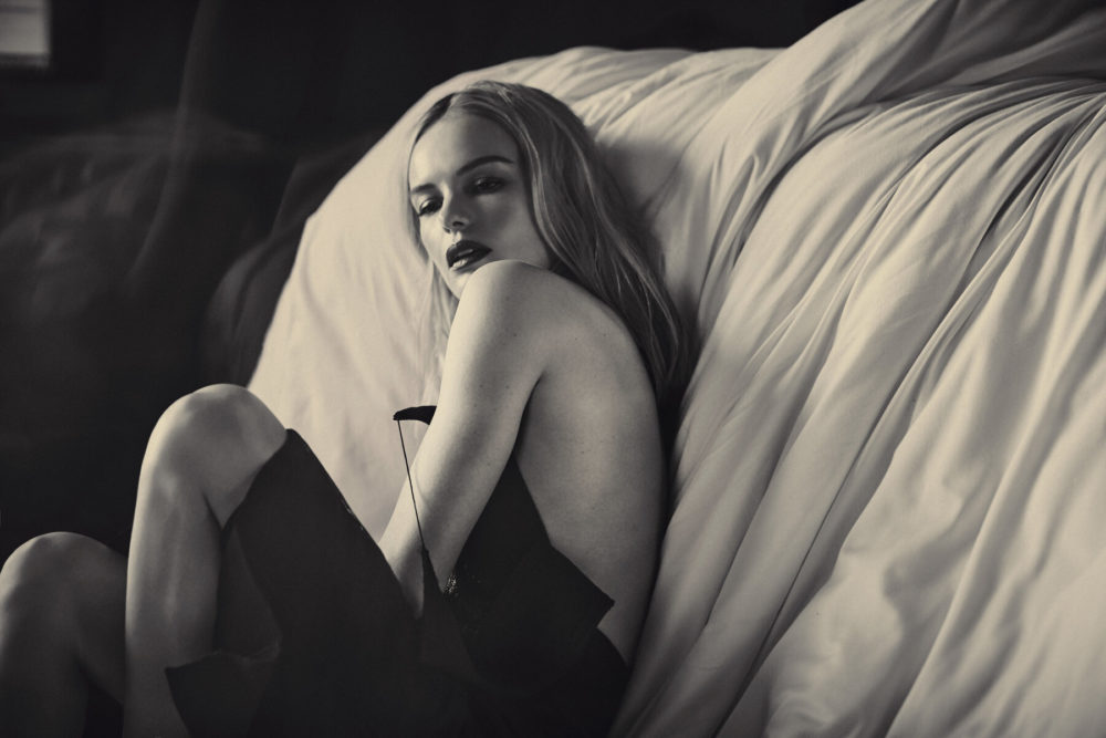 Kate Bosworth by Guy Aroch, black and white portrait of the actress in a black slipdress sitting next to a bed with white sheets