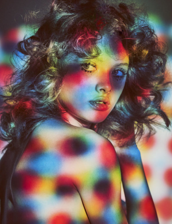 Naked by Guy Aroch, portrait of nude model in sixties style makeup and curly hair, covered in colorful light dots