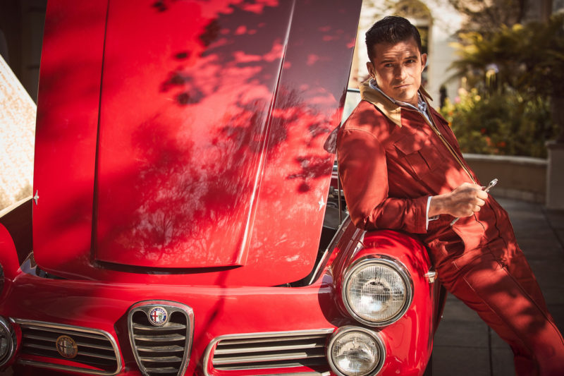 Orlando Bloom II by Guy Aroch, the actor in a red onepiece holding a wrench and leaning on a red oldtimer car with open engine hood