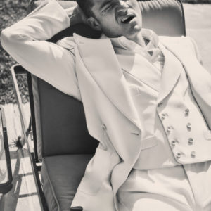 Orlando Bloom by Guy Aroch, the actor in a white suit lying on a sun lounger pulling a grimace