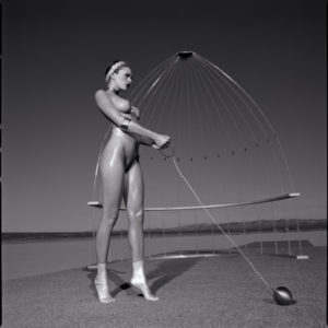 OLYMPIC SHOT PULL b&w by Guido Argentini, nude model in metallic socks about to throw a metal ball