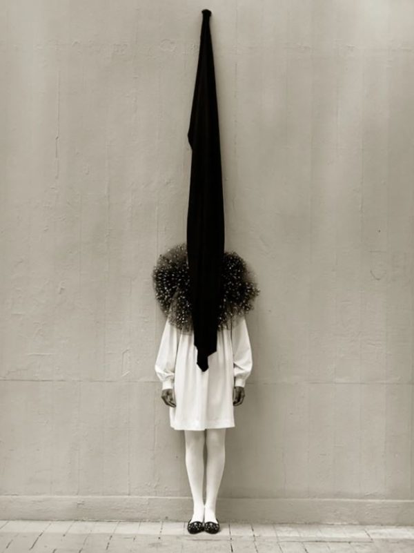 Leslie Weiner in Yohji by Albert Watson, girl in white dress and tight with black tulle ruff standing in front of a grey wall with a black piece of fabric hanging over her face