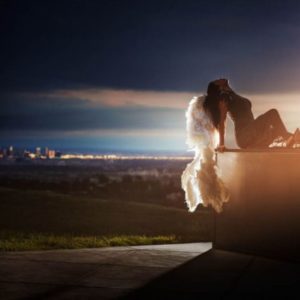 City of angels by David Drebin, model with white feather wings sitting on a foreground, a skyline by night in the background