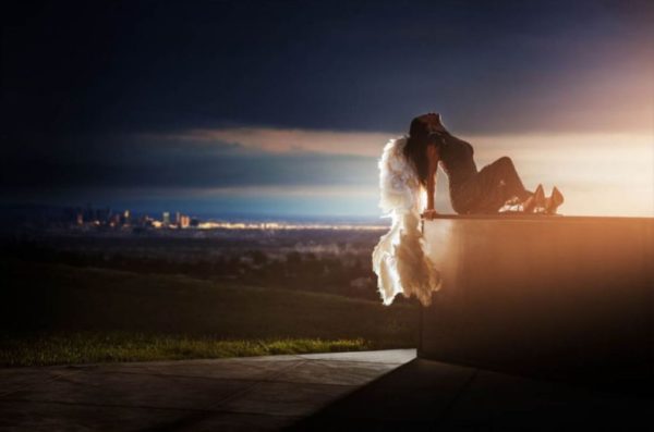 City of angels by David Drebin, model with white feather wings sitting on a foreground, a skyline by night in the background