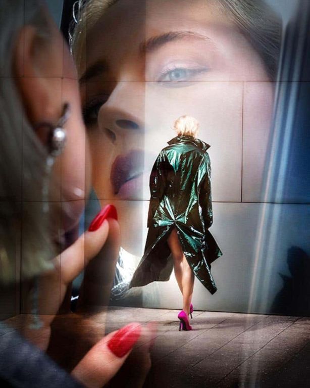 Facing myself by David Drebin, double exposure of model looking at herself in the morror and model in a shimmering green coat walking away