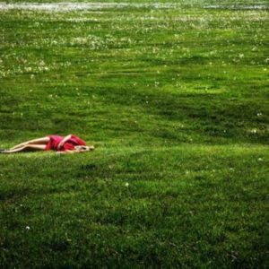 Field of dreams by David Drebin, model in red dress lying in green meadow on the grass