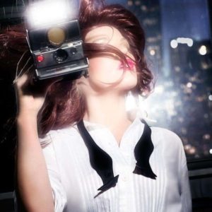 Flashing girl by David Drebin, model in white shirt and open bowtie holding an instant camera and blitzing at the camera