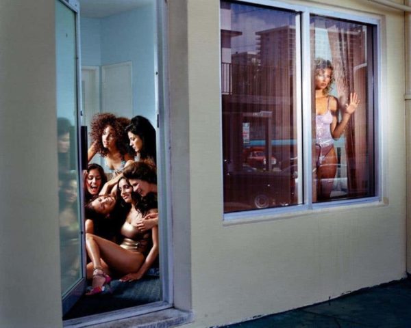Gina and the rivals by David Drebin, model in purple lingery looking out of a mirror while a group of models is sitting nextdors