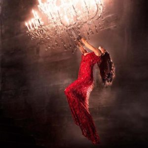Hanging on by David Drebin, model in red dress hanging from a crystal chandelier