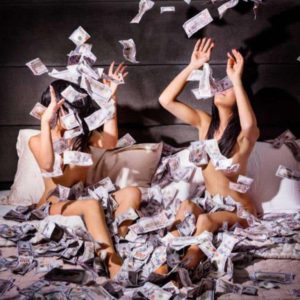 Money shot by David Drebin, two models sitting in bed, 100 dollar bills flying around them