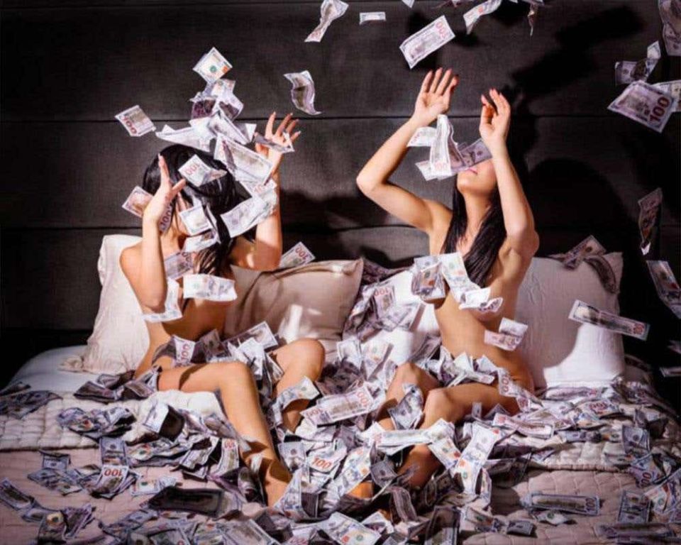 Money shot by David Drebin, two models sitting in bed, 100 dollar bills flying around them