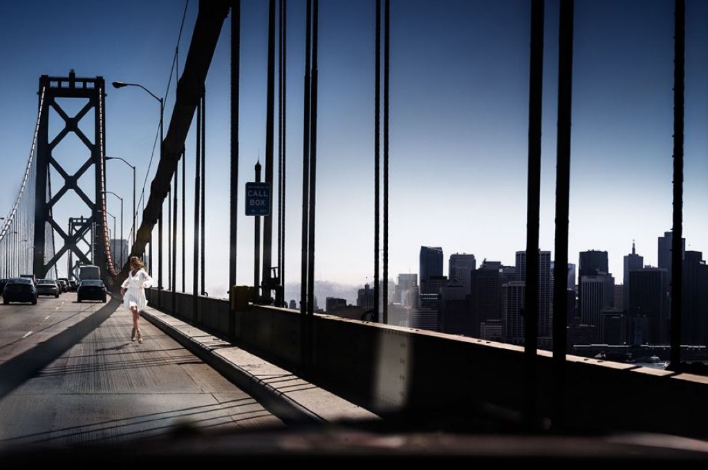 Running the bride by david drebin, model in white dress running over the san francisco bay bridge, the city in the backgrond