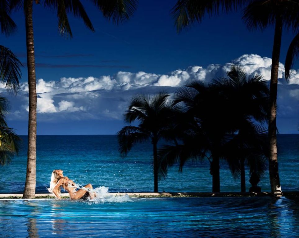 Splasher in paradise by David Drebin, nude model sitting on a beach between palm trees, splashing in the water