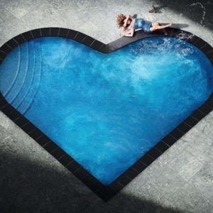 Splashing heart by David Drebin, model in short blue glitter dress lying next to heart shaped pool, splashing water with her foot
