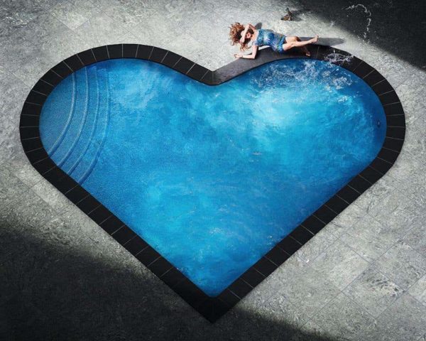 Splashing heart by David Drebin, model in short blue glitter dress lying next to heart shaped pool, splashing water with her foot