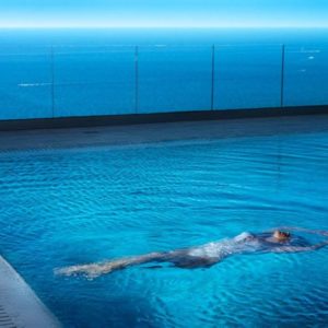 The escapist by David Drebin, model in white bathing suit floating in a pool next to the ocean