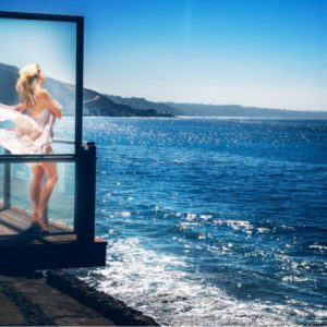 The ocean blond by David Drebin, model in flowing white dress standing on a balcony over the ocean