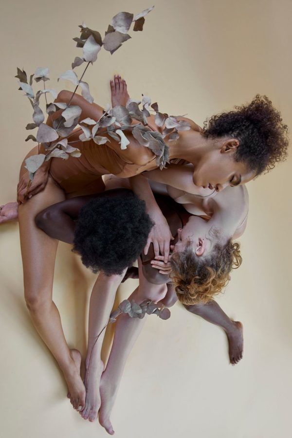 3 Grace praying by Iris Brosch, three models with different skintones, wearing nude leotards, sitting on the floor intertwined and holding eucalyptus twigs