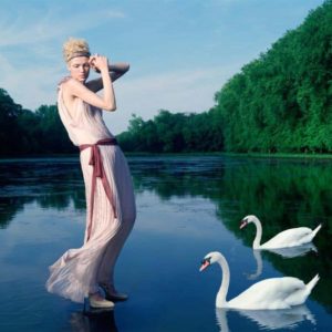Girl with swans for Greek Vogue by Iris Brosch, model in transparent pink draped dress standing on a lake with two swans