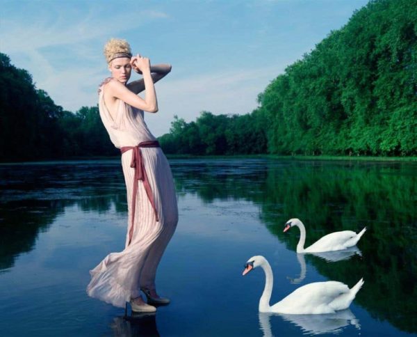 Girl with swans for Greek Vogue by Iris Brosch, model in transparent pink draped dress standing on a lake with two swans