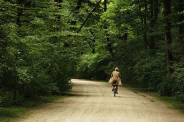 Germany by Marc Baptiste, person in a trenchcoat riding a bike through the forest