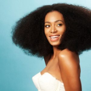 Solange Knowles by Marc Baptiste, portrait of the singer wearing her afro and a white bustier, in front of a turquoise background