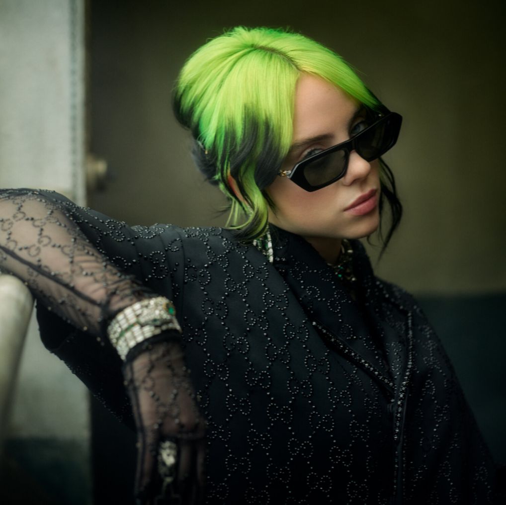 Billie Eilish by Mark Seliger, portrait of the singer with green and black hair, wearing sunglasses and a black gucci shirt with matching gloves