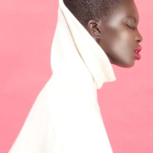 Ashock by Sylvie Blum, sideprofile of a black model in a white turtleneck and red lip with pink background