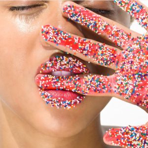 Candy fingers by Sylvie Blum, closeup portrait of modl holding her hand in front of her face, finger between her teeath, hand and lips covered in