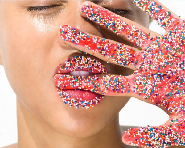 Candy fingers by Sylvie Blum, closeup portrait of modl holding her hand in front of her face, finger between her teeath, hand and lips covered in sugar sprinkles