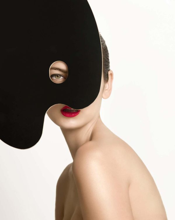 Hanna One by Sylvie Blum, portrait of unde model in red lip, a black shape covering hr face so only one eye and her mouth are visible