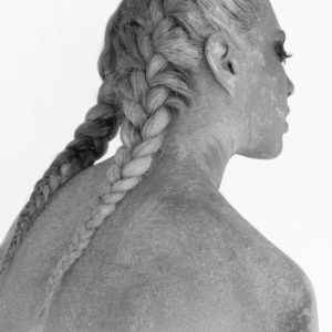 Leila by Sylvie Blum, black and white portrait of a model in braids, covered in white dust, turning her back to the camera