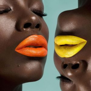 Pop Lips One 201 by Sylvie Blum, closeup of two black models with bright roange and yellow lips, one of them upside down