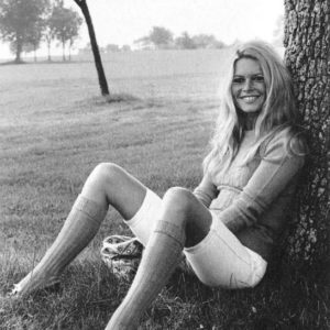 Brigitte Bardot by Terry O'Neill, the model in white shorts and kneehigh sokks leaning against a tree on a meadow