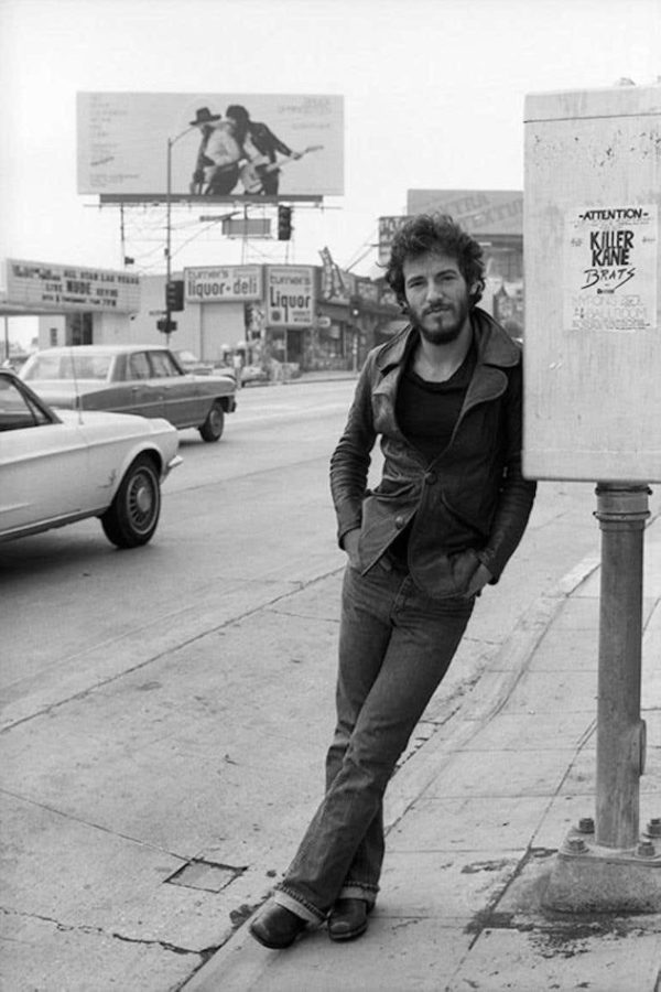 Bruce Springsteen by Terry O'Neill, the musician leaning against a post with cars, a liquor store and a poster in the background