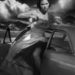 Adriana Lima by Vincent Peters, the model in white dress, stepping out of a vintage car, hills and clouds in the background