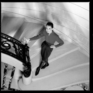 Audrey Hepburn by Timothy white, the actress in black skirt and kitten heels posing on a staircase with cast iron railing