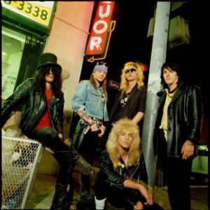 Guns n Roses by Timothy White, the band posing next to a shops neon signs and a trash can