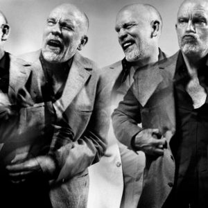 John Malkovich by Vincent Peters, four portraits of the actor in a grey suit, pulling faces