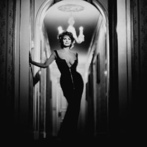 Raquel Welch by Timothy White, the actress in black, lowcut gown standing in historicist hallway