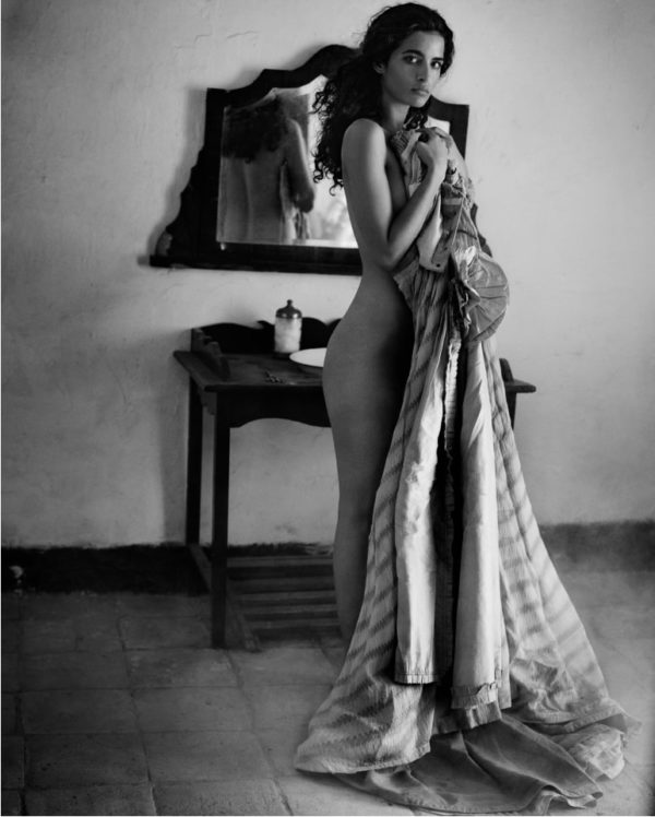 Sicily Palermo by Vincent Peters, a model with dark courls standing in front of a rustic vanity, nude, covering her body parsially with striped fabric