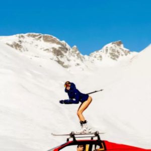 Off Piste by Tony Kelly, Model in blue jacket on ski on top of a res Ferrari in the snowy mountains