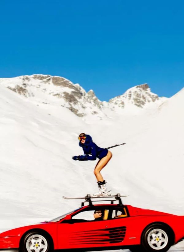 Off Piste by Tony Kelly, Model in blue jacket on ski on top of a res Ferrari in the snowy mountains