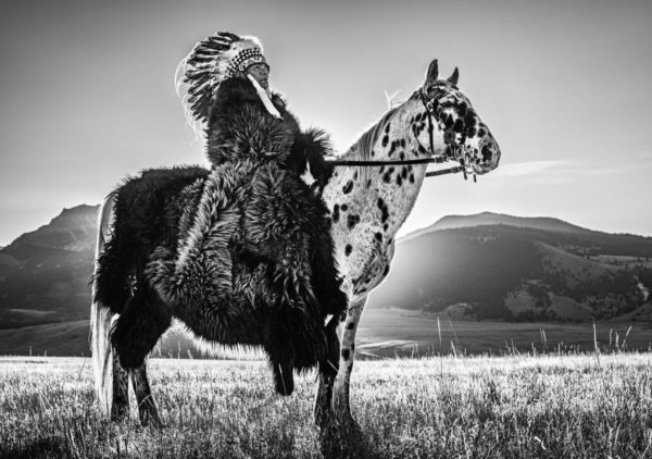 Lakota by David Yarrow, Native Chieve with feather headpiece and fur coat sitting on leopard horse