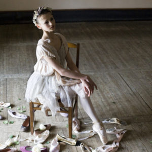 Christina Shapran by Arthur Elgort, ballerina in tutu and flowercrown sitting on a chair between shoes
